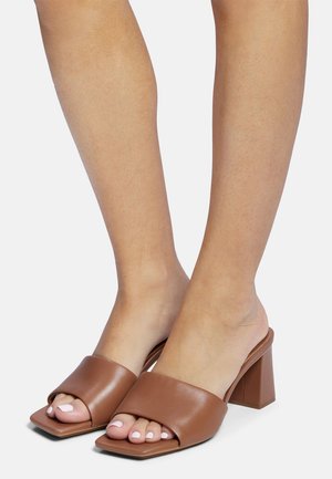 Mule in pelle marrone con punta quadrata, apertura sul retro e fascia larga. Presenta un tacco a blocco, texture liscia e piedi scoperti.