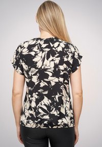Schwarz- und cremefarbene Bluse mit Blumenmuster und kurzen Ärmeln, entspanntem Schnitt und runder Halslinie. Sie verfügt über leicht geraffte Details auf der Rückseite.