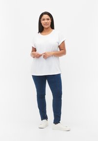 Camiseta blanca de manga corta con cuello redondo, combinada con unos jeans ajustados de color azul oscuro y zapatillas blancas. Atuendo simple y casual.