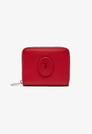 Rode leren portemonnee met ritssluiting rondom en een gestikt ovaal embleem met een kleine abstracte uitsparing in het midden.