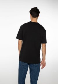 Zwarte korte mouwen t-shirt met een ronde hals, met een ontspannen pasvorm en een zachte textuur. Gecombineerd met blauwe denim jeans.