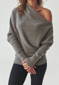 Warmes graues, oversized Sweatshirt mit einem schulterfreien Design, gerippten Bündchen und einer lockeren Passform. Die weiche Textur ergänzt den lässigen Stil.