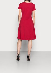 Czerwona sukienka z krótkim rękawem o dopasowanej górze, rozkloszowanej spódnicy i gładkiej fakturze, w połączeniu z czarnymi szpilkami.