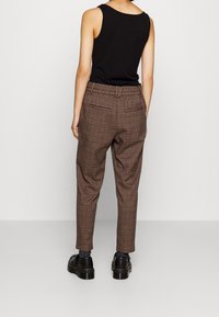 Bruna rutiga byxor med avslappnad passform, utrustade med resårmidja och bakfickor. Matchas med svarta skor och strumpor.