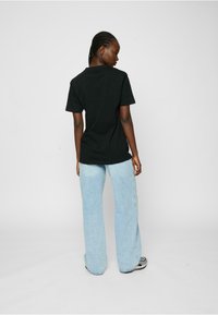 Black t-shirt with short sleeves paired with light blue flared jeans. Smooth fabric, relaxed fit, and minimalistic design.