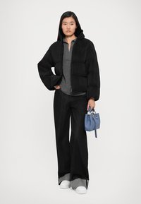Black puffer jacket with ribbed texture, gray long-sleeve shirt, wide-leg dark jeans, white sneakers, and a small blue handbag.