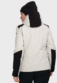 Weiße und schwarze wasserdichte Jacke mit Kapuze, die kontrastierende Schulterpaneele und eine glatte Textur aufweist. Begleitet von einer schwarzen Mütze.