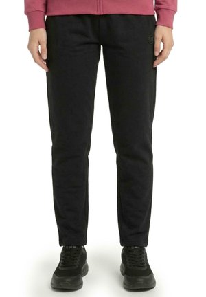 Modèle portant un pantalon noir à jambes droites et des baskets noires, avec un sweat-shirt bordeaux, sur fond blanc.