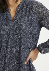 Marineblauwe blouse met een bloemenpatroon, v-hals en lange mouwen. Gemaakt van lichtgewicht stof, met een ontspannen pasvorm en subtiele plooidetails.