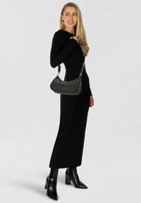 Schwarze Lederhandtasche mit geschwungener Form und goldfarbenen Beschlägen, getragen an einem Schulterriemen, kombiniert mit einem taillierten schwarzen Kleid und Stiefeln.