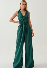 Completo verde senza maniche con scollatura a V, vita regolabile con stringa e design a gamba larga. Tessuto morbido, materiale liscio senza motivi.