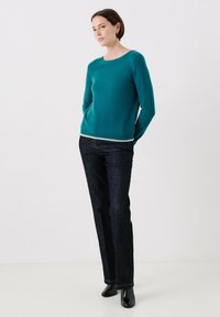 Maglione teal in un materiale morbido con collo rotondo, abbinato a jeans denim scuri e stivaletti neri. Design semplice con un leggero bordino.