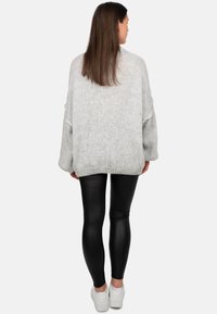 Maglione grigio chiaro oversize in maglia, con maniche ampie e orlo a coste, abbinato a leggings neri con effetto pelle e sneakers bianche.