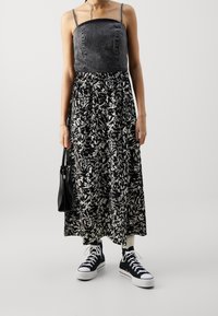 Denim bodice dengan paku perak, rok maxi berpola bunga hitam-putih, dipadukan dengan sepatu sneaker hitam dan tas kecil hitam.