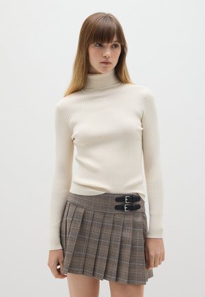 Maglione a collo alto a coste color crema con maniche lunghe abbinato a una gonna plissettata a quadri con dettagli a doppia fibbia nera.