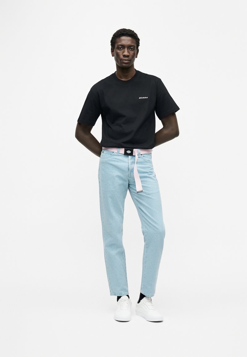 Camiseta negra de algodón con texto, jeans azul claro con cinturón rosa y zapatillas blancas. Diseño sencillo, ajuste relajado y sin patrones visibles.