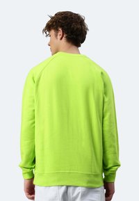 Felpa in cotone verde neon con polsini e orlo a costine, scollatura a girocollo e vestibilità rilassata. Presenta una texture liscia e maniche lunghe.
