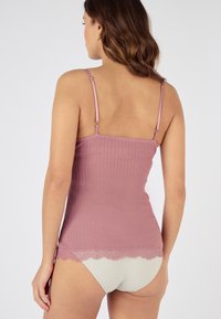 Top scollato lilla a coste con spalline sottili, con un bordo in pizzo all'orlo e tessuto liscio. Indossato con una biancheria intima di colore chiaro.