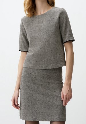 Femme portant un haut gris à manches courtes avec un motif en chevrons et une jupe assortie sur un fond uni.