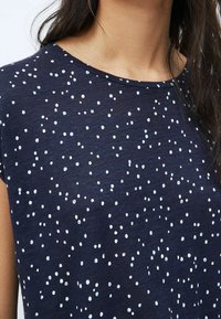Navy t-shirt with a round neck, short sleeves, and a scattered white dot pattern. Soft fabric with a slightly textured finish.