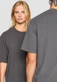 Sivý oversize tričko s okrúhlym výstrihom. Krátke rukávy, bavlnený materiál, jemná textúra. Zobrazené na dvoch postavách, predný a zadný pohľad.