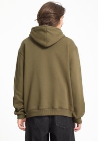Oliven grøn hættebluse med løs pasform, ribstrikkede manchetter og kant samt en kængurulomme. Stoffet virker blødt med en glat tekstur.