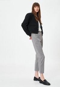 Chaqueta negra corta con grandes bolsillos, camisa blanca, pantalones grises ajustados de tejido suave y mocasines de charol negros.