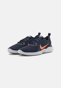 Chaussures de sport en mesh bleu marine avec le swoosh orange de Nike, bout arrondi, accents gris et semelle blanche. Équipées de lacets et d'une languette pour un enfilage facile.