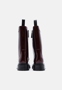 Μποτάκια αστραγάλου από βουργουνδί δερμάτινο γυαλιστερό, με χοντρή μαύρη σόλα, φερμουάρ και θηλιές στο πίσω μέρος για εύκολη εφαρμογή.