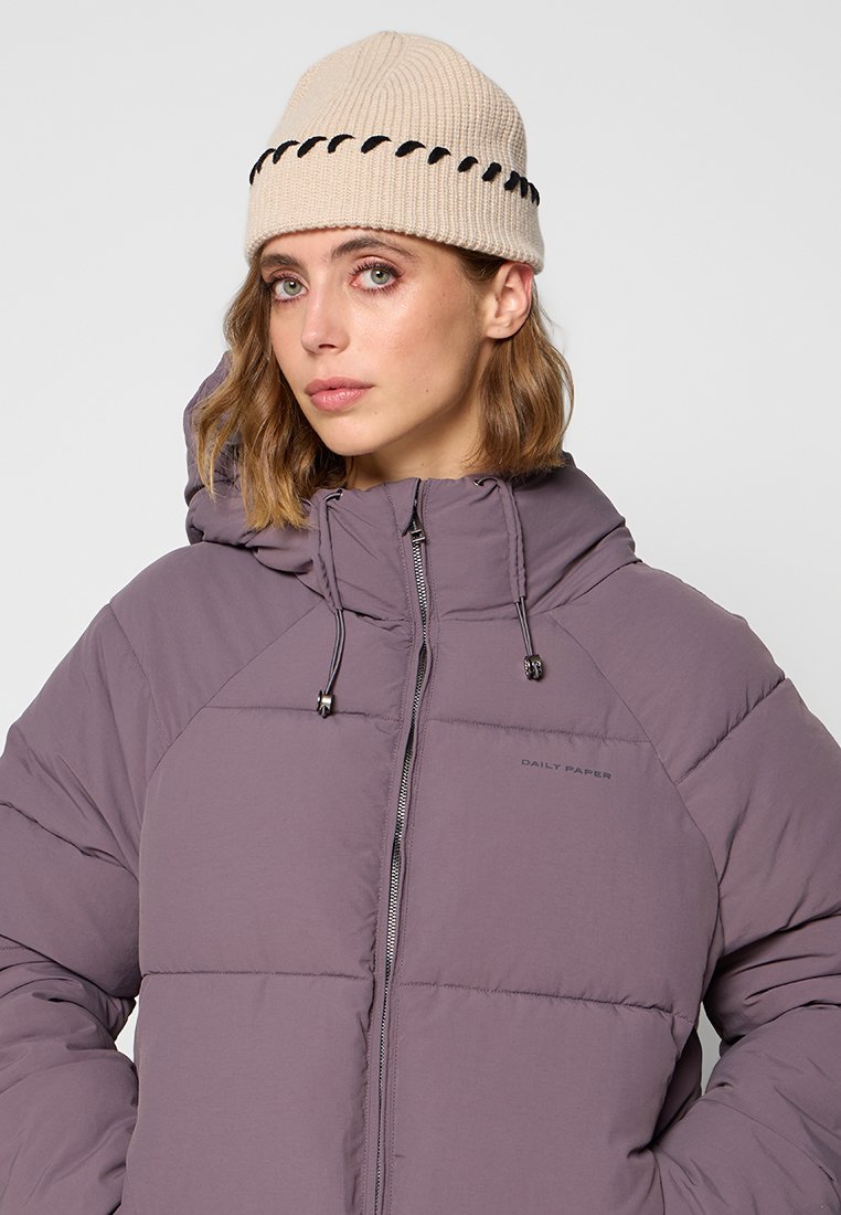 Lila Puffjacke mit Reißverschluss und Kordelzugkapuze, kombiniert mit einer beigen Strickmütze mit schwarzen Akzentnähten.