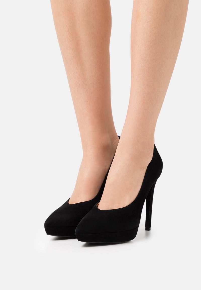 Chaussures à talons hauts en suede noir avec un bout arrondi et une découpe basse. Elles sont dotées d'une plateforme et d'un talon aiguille mince.