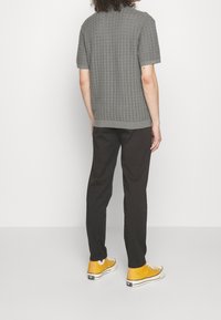 Grå strikket kortærmet sweater med et struktureret design, kombineret med sorte bukser og gule sko. Sweateren har en rund halsudskæring og ribbet kant.