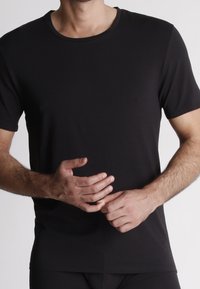 T-shirt nera a maniche corte realizzata in un materiale liscio, con scollatura a girocollo e una forma aderente, senza motivi o rifiniture visibili.