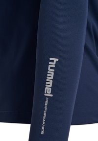 Marinblå långärmad träningsskjorta med ribbad struktur, med en silverfärgad logotyp och texten "hummel PERFORMANCE" på vänster ärm.