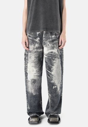 Person wearing loose, faded black and gray distressed pants with a black sleeveless top and square-toed black shoes.