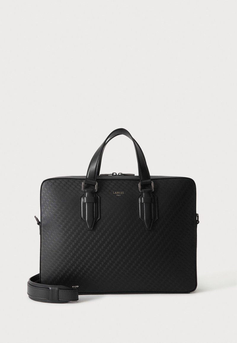 Черно куфарче Lancel Paris с текстурирана повърхност, две дръжки, горен цип и сваляща се презрамка на светъл фон.