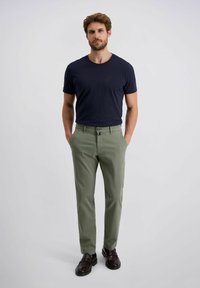 Marineblaues T-Shirt, kombiniert mit hellgrünen Hosen. Die Hose verfügt über einen Knopfverschluss und Taschen, während braune Anzugschuhe das Outfit abrunden.