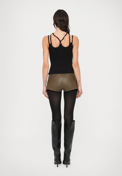 Top preto justo com alças finas, combinado com calções de couro verde-oliva, collants pretos transparentes e botas pretas altas.