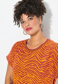 Camiseta de manga corta y cuello redondo en color naranja con rayas de cebra en amarillo y burdeos. Tejido suave con una textura lisa.