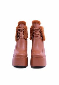 Stivali platform in finta pelle marrone con suola chunky, dotati di soffici accenni marroni attorno alla caviglia e lacci per una chiusura sicura.