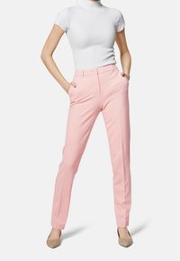 Pantaloni su misura rosa chiaro con tasche laterali, design aderente e texture sottile, abbinati a un top bianco a coste a maniche corte.