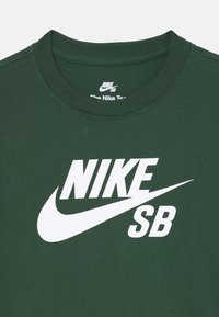 Grünes Baumwoll-T-Shirt mit großem weißen Nike SB-Logo und Swoosh-Design, Rundhalsausschnitt und kurzen Ärmeln. Strukturierter Stoff.