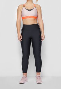 Reggiseno sportivo rosa chiaro con fascia arancione, abbinato a leggings neri a vita alta con accenti bianchi sui lati. Scarpe da ginnastica rosa.