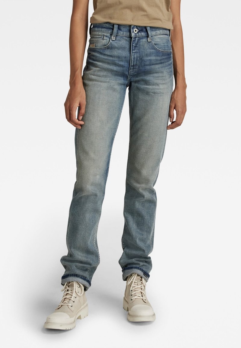 Jeans de pierna recta azul claro, hechos de denim, con un lavado desgastado y detalles de costura sutiles. Combinados con botas beige de cordones.