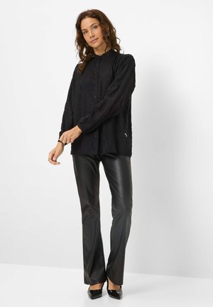 Chemise noire à manches longues avec des boutons en tissu texturé, associée à un pantalon en simili cuir noir ajusté et des escarpins noirs à bout pointu.