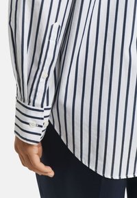 Gestreiftes Langarmshirt in Weiß und Marineblau mit geknöpften Manschetten. Verfügt über einen klassischen Kragen und ein weiches Baumwollgewebe.