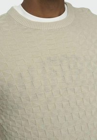 Pull en tricot beige clair avec un motif en losanges texturé, doté d'un col rond côtelé et d'une couche intérieure lisse.