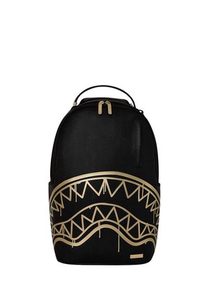 Zaino nero con cerniera dorata e un grande motivo di denti di squalo dorati sulla pannello frontale.