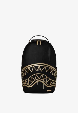 Mochila negra con cremallera dorada y un diseño grande de dientes de tiburón dorados en el panel frontal.