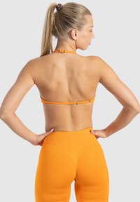 Sostén deportivo naranja con tirante trasero ajustable, combinado con leggings naranjas de tiro alto, ambos con una textura suave.